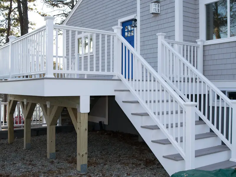 Elevated deck with white railing and staircase leading to a blue front door